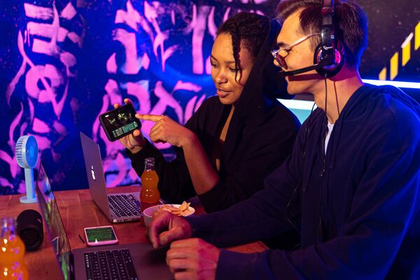 Two people wearing headphones looking at a mobile game on a screen in a purple lit room