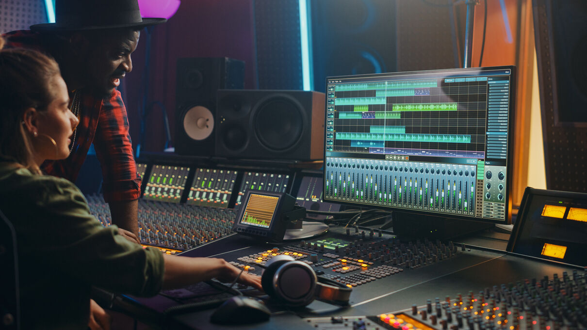 Two people working surrounded by audio editing equipment