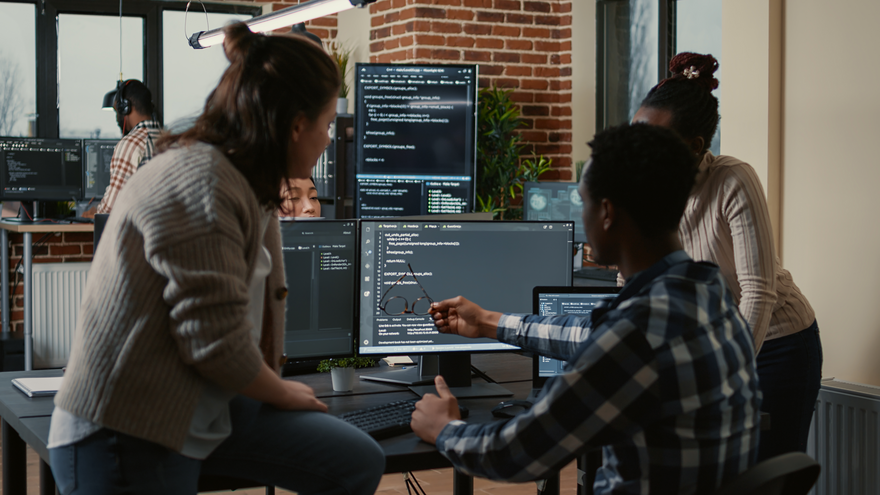 Three people working on a computer running code