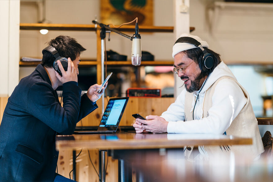 two men wearing headphones either side of a microphone