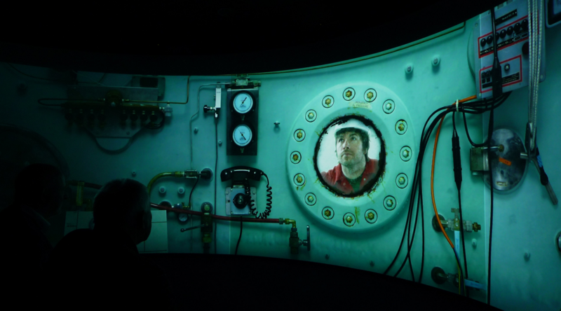 Immersive digital screen showcasing a submarine, at the centre a man lookin out.