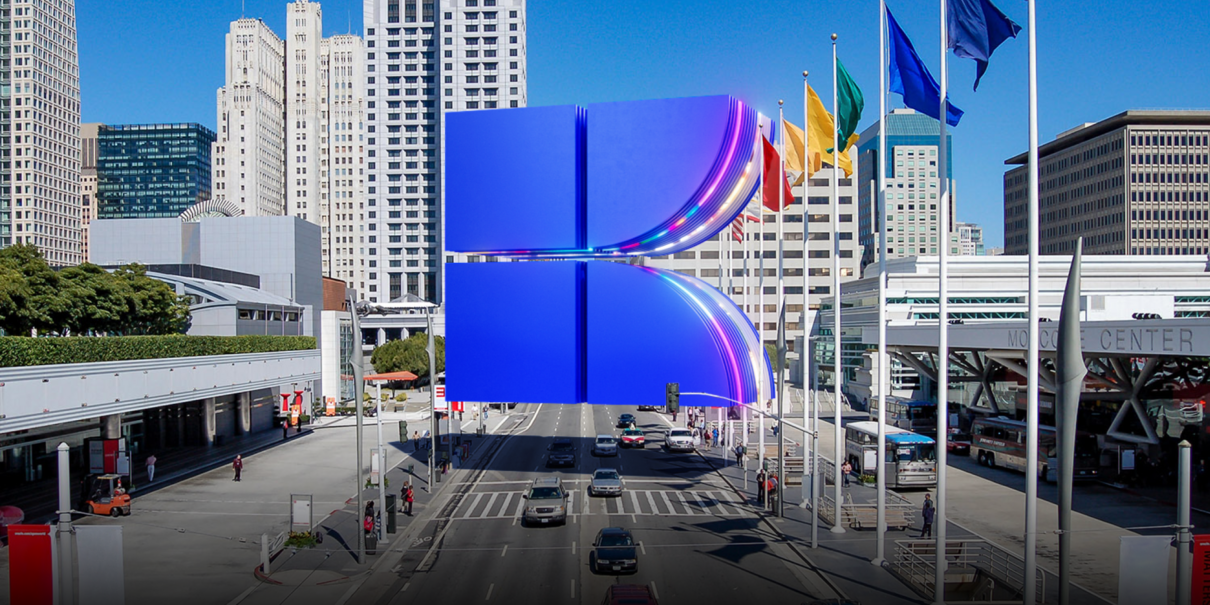 Urban skyline with skyscrapers, colorful flags, and a large blue K over San Francisco street