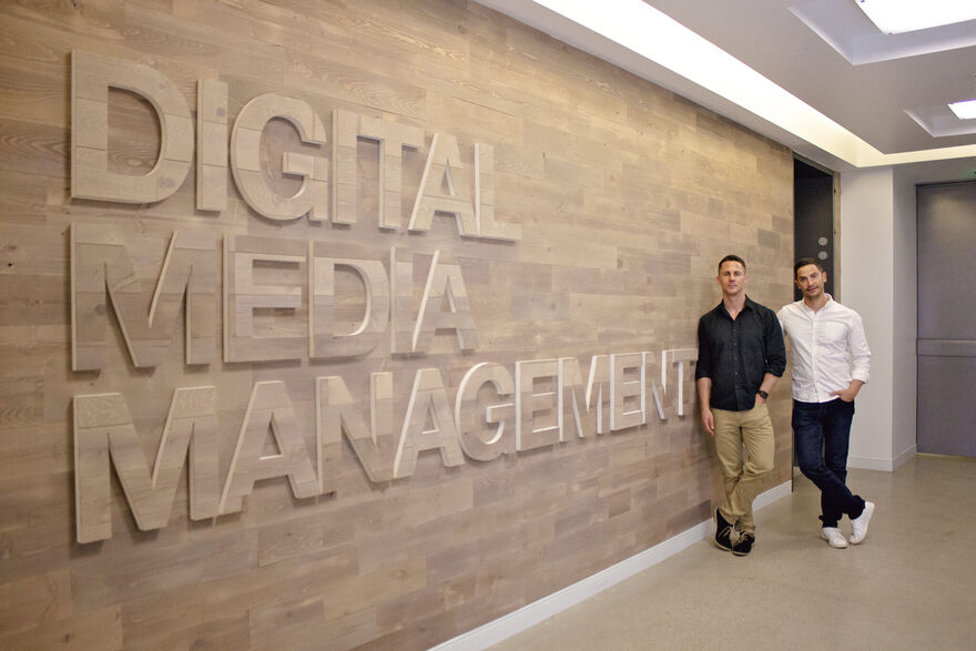 two men standing by the Digital Media Management logo which is on a wall