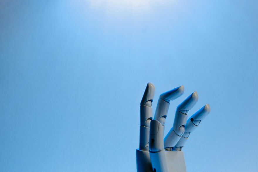 Robotic hand reaching upward against a bright blue sky.
