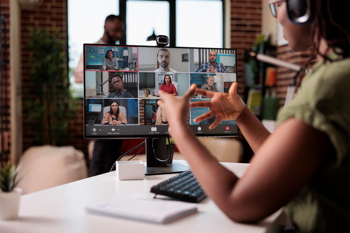 A woman on a computer in a video call with 9 peopkle